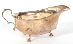 A hallmarked silver sauce boat of typical form with wavey rim, scroll capped handle on three hoof