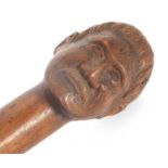 A vintage carved hardwood walking stick, carved with a mans head having a moustache and Maori type