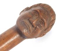 A vintage carved hardwood walking stick, carved with a mans head having a moustache and Maori type