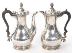 A George V silver coffee pot and hot water jug of baluster form, hinged urn finials and black wooden