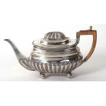 A George III teapot with a part lobed body with applied gadrooned border and wooden handle supported