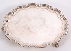 A George V silver salver of plain design with pie crust edge, supported on three scroll feet,