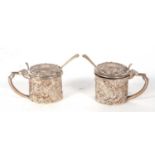 A pair of small Edwardian silver mustards of drum form embossed all over with scrolled design,