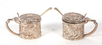 A pair of small Edwardian silver mustards of drum form embossed all over with scrolled design,