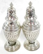 A pair of Victorian silver peppers, the urn shaped bodies with a wrythen design having urn finials
