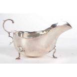 A George V silver sauce boat of typical form having wavey rim and flying scrolled handle,