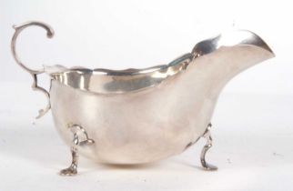 A George V silver sauce boat of typical form having wavey rim and flying scrolled handle,