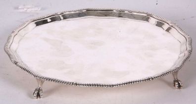 A George V silver salver having an applied shaped gadrooned rim on plain ground, supported on four
