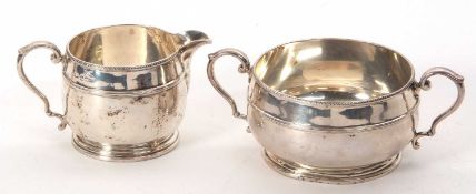 A George V silver matching cream jug and twin handled sugar bowl of squat baluster form, beaded