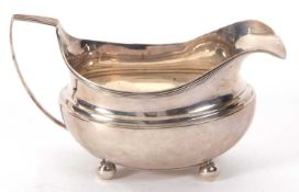 A George III silver cream jug of oval form having reeded edge and handle, supported on four ball