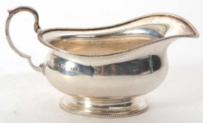 A George V silver cream jug of plain oval form applied gadrooned rims, capped leaf handle,
