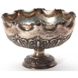 A late Victorian silver pedestal bowl having a crimped edge, the body elaborately embossed with