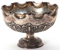 A late Victorian silver pedestal bowl having a crimped edge, the body elaborately embossed with