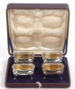 A cased set of four George V salts of oval form, applied shell and gadrooned edges, supported on