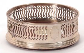 An Elizabeth II silver wine bottle coaster having a pierced geometric design, the treen base with