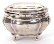 An Edwardian silver oval caddy of plain serpentine form, having a hinged lid and supported on four