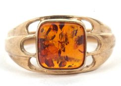 A 9ct amber ring, the square amber cabochon, collet mounted with pierced scalloped shoulders and