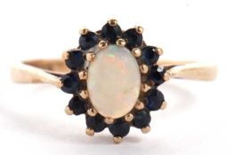 A 9ct sapphire and opal cluster ring, the central oval opal cabochon surrounded by small round