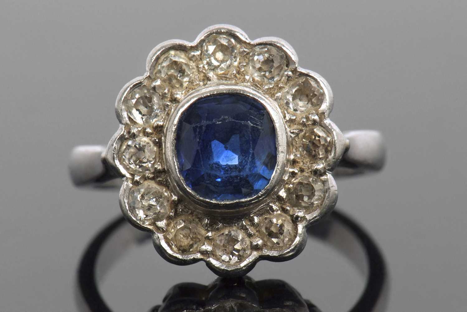 A sapphire and diamond cluster ring, the cushion shaped faceted sapphire is 7x7x4mm approx, bezel