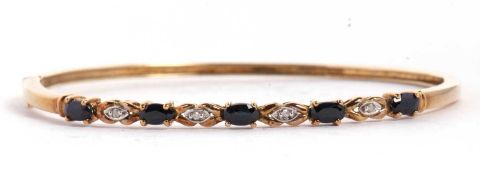 A sapphire and diamond hinged bangle, set with five oval claw mounted sapphires, interspaced with