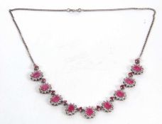 A ruby and white topaz necklace, comprised of 9 oval rubies surrounded by round white topaz, each