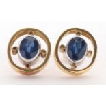 A pair of sapphire earrings, the oval sapphires in white metal collet mounts, set within an open