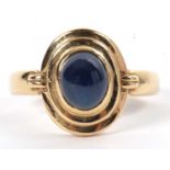 An 18k sapphire ring, the round cabochon sapphire, collet mounted within a stepped frame, with plain