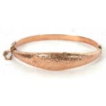 An early 20th century rose gold hinged bangle, the tapered upper half with engraved decoration