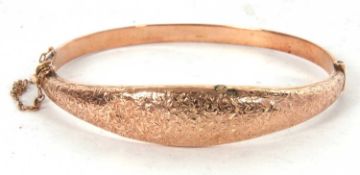 An early 20th century rose gold hinged bangle, the tapered upper half with engraved decoration