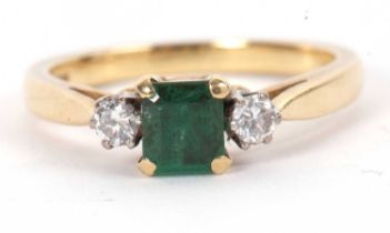 An emerald and diamond ring, the central square emerald cut emerald in a four claw mount with a