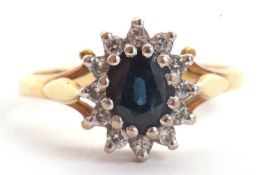 An 18ct sapphire and diamond cluster ring, the oval deep blue sapphire surrounded by small round