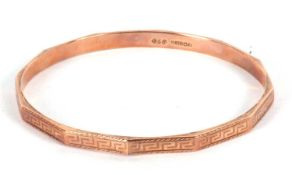 A 9ct rose gold bangle, with faceted design to outer ring with engraved Greek key decoartion,