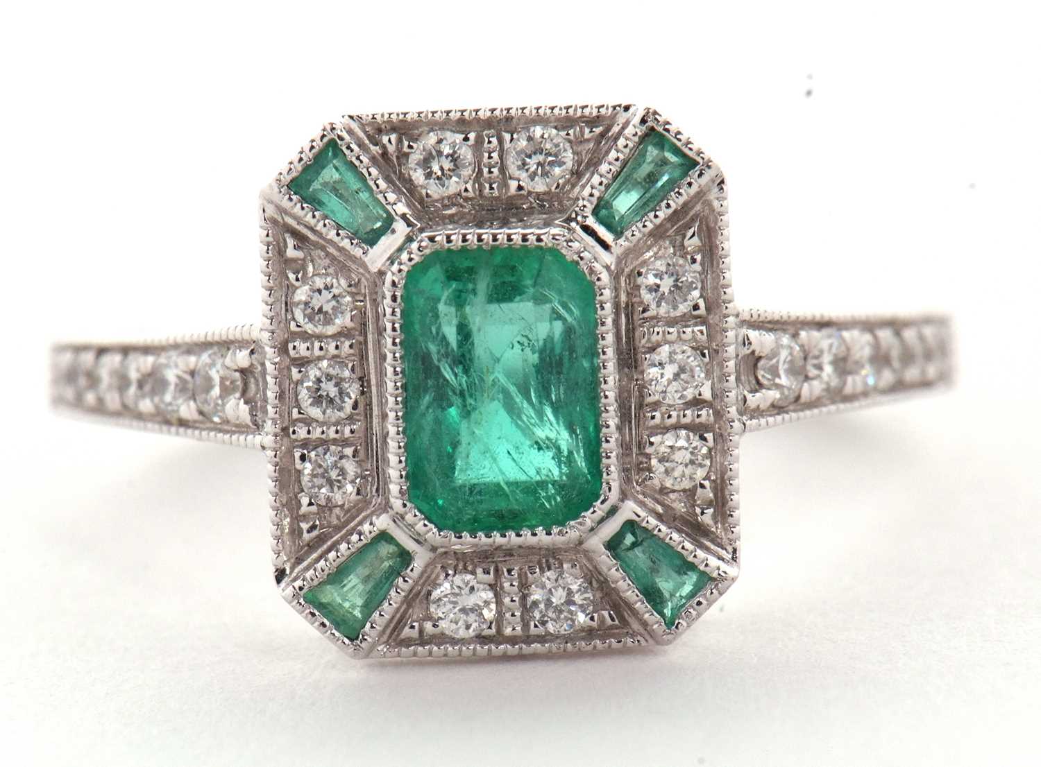 An 18ct emerald and diamond Art Deco style ring, the central emerald cut emerald surrounded by small