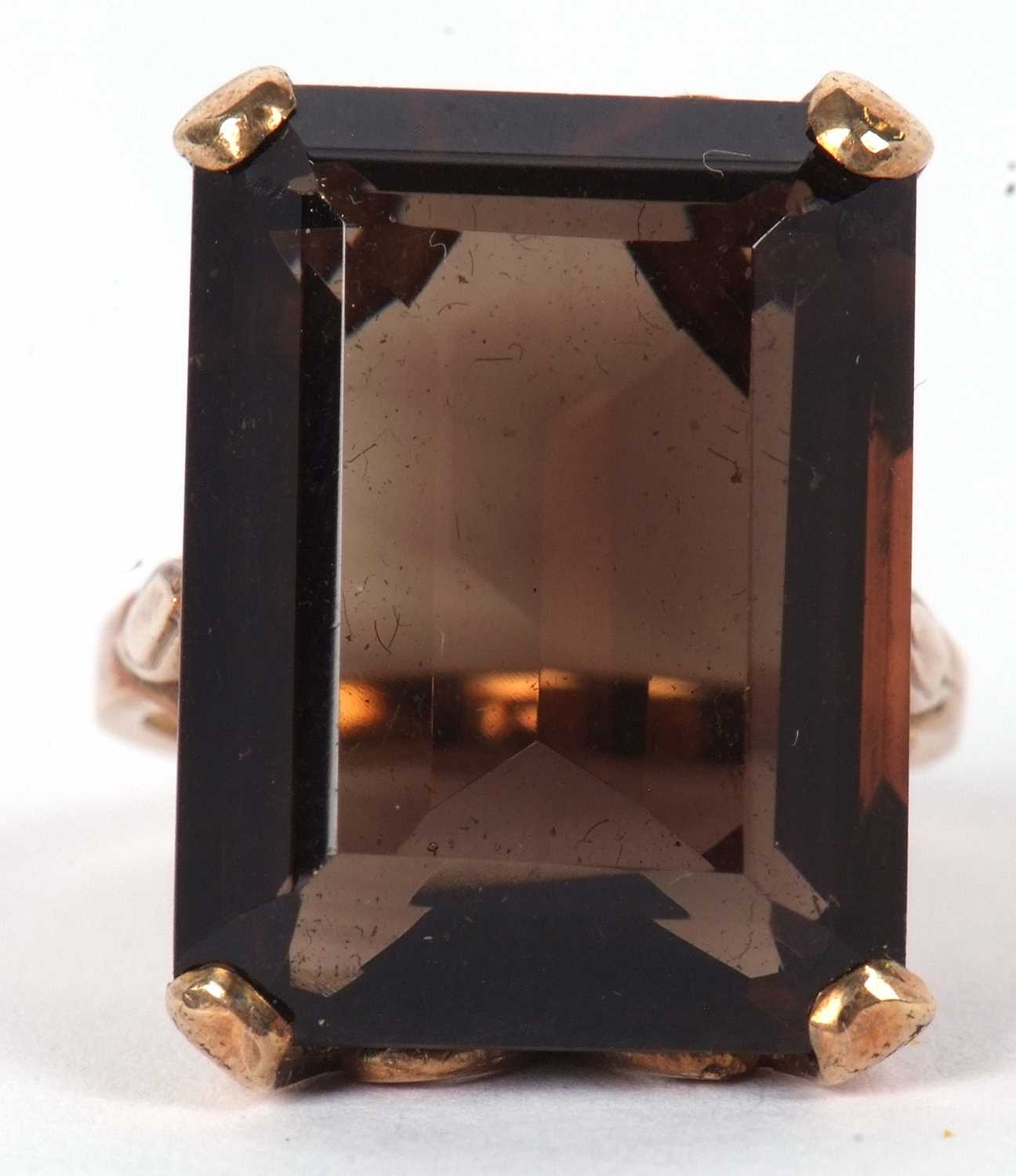 A 9ct smokey quartz ring, the emerald cut mokey quartz in a four claw mount and scrolled gallery,