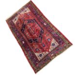 20th Century Pakistani wool floor rug decorated with a large central lozenge on a principally red