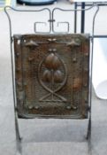 An Arts & Crafts style iron framed fire screen inset with a copper panel with stylised floral