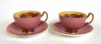 Two Aynsley cups and saucers with pink exterior ground, the interior printed with fruit