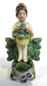 A small pearl ware late 18th Century figure of a cherub holding flowers against bocage
