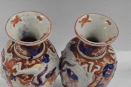 A pair of Japanese porcelain vases in Imari type designs with dragons modelled in relief, 28cm high