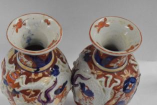 A pair of Japanese porcelain vases in Imari type designs with dragons modelled in relief, 28cm high