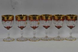 A group of Italian crystal wine glasses with purple overlay and gilt design above a knopped stem,