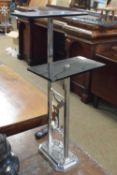 An Art Deco style chrome and black glass two tier stand with figural decoration, 63cm high