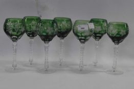 A group of seven wine glasses, the green coloured bowls with an engraved design above a faceted
