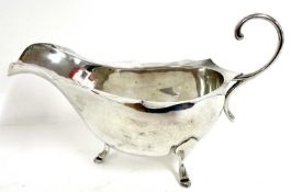 White metal sauce boat with card cut rim having a flying scroll leaf handle supported on three feet,