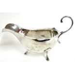 White metal sauce boat with card cut rim having a flying scroll leaf handle supported on three feet,