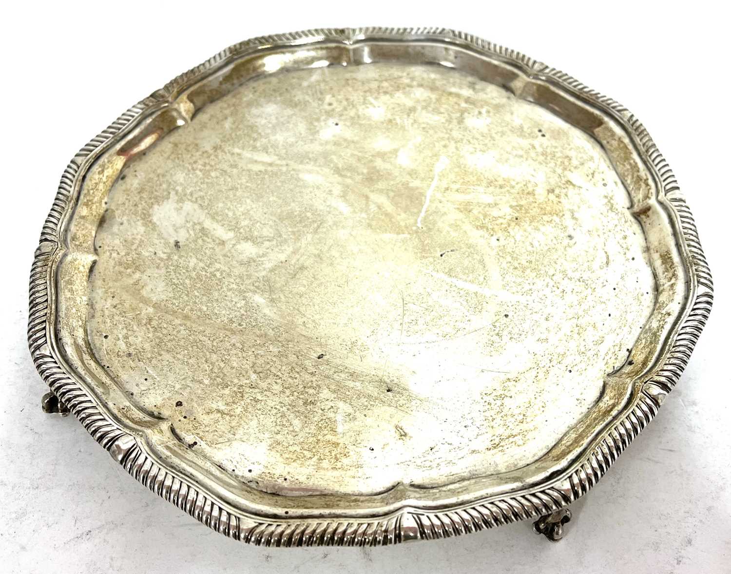 George V silver salver, the scalloped rim with gadrooned border supported on four claw and ball