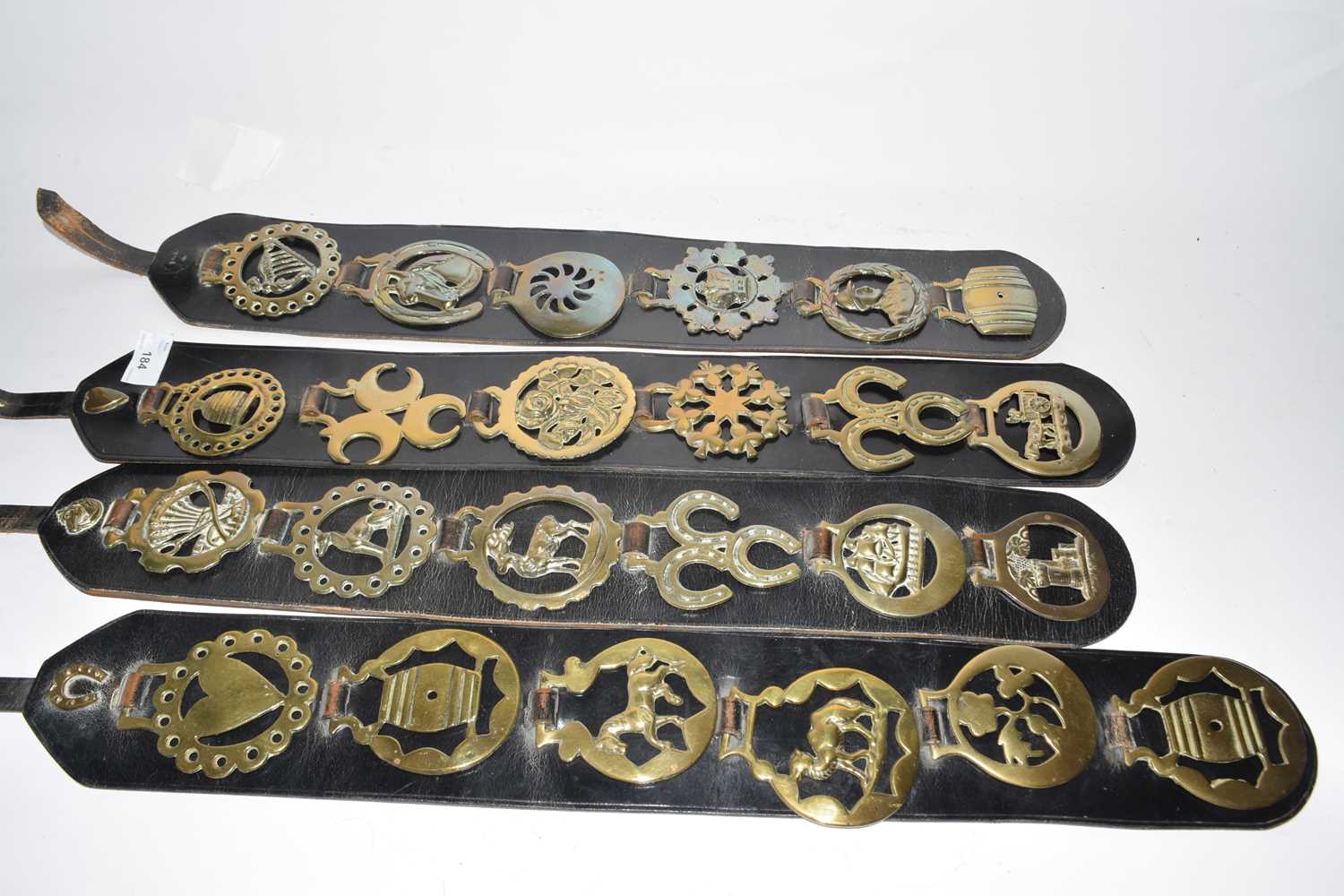 Four leather straps containing various assorted horse brasses
