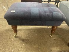 A modern upholstered footstool with turned legs and casters