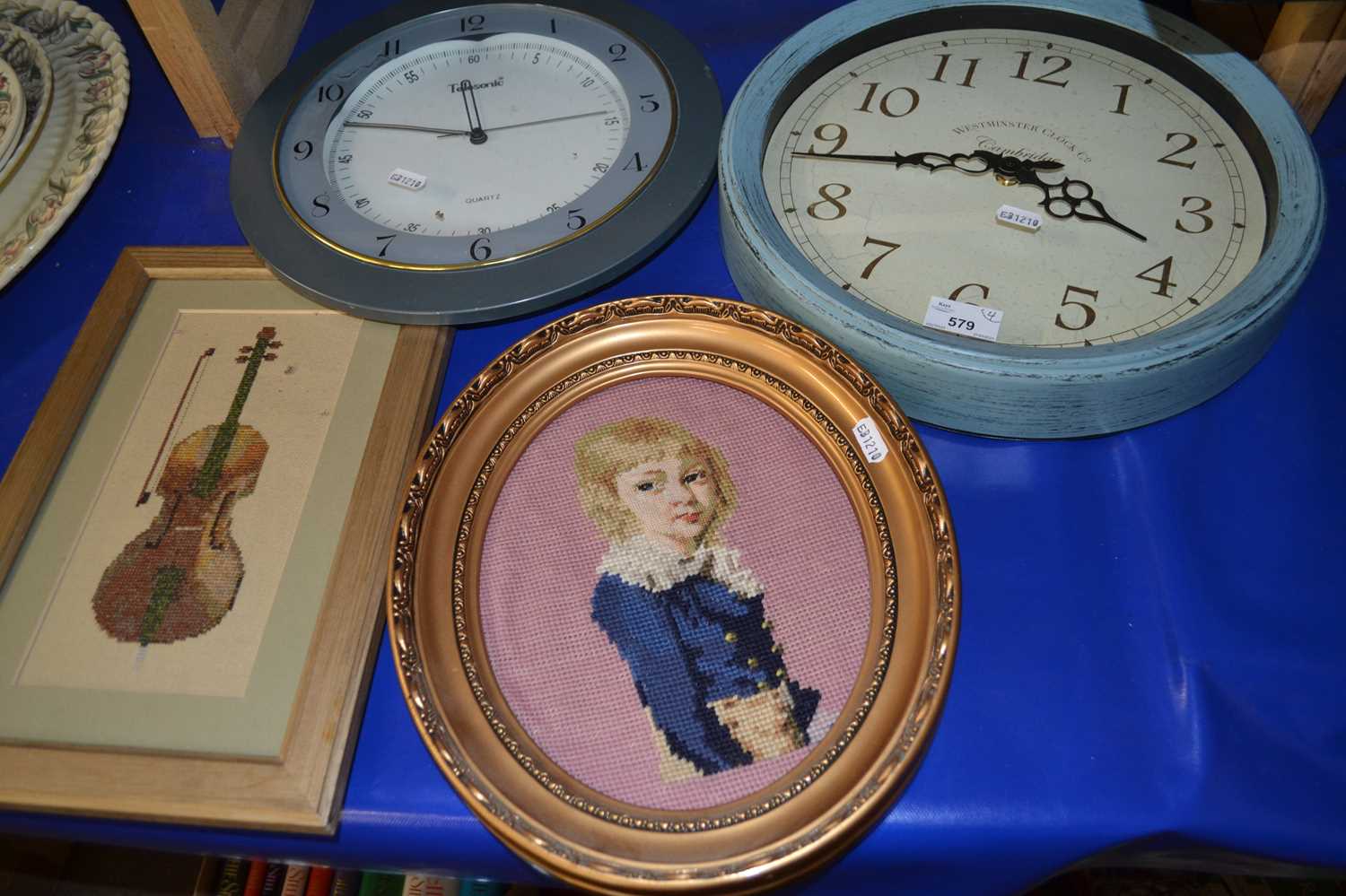 A duck egg blue wall mounted wall clock together with another and two needlework pictures