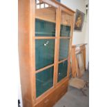 Light oak gun cabinet with two glazed doors and drawers to base, the interior with green baize